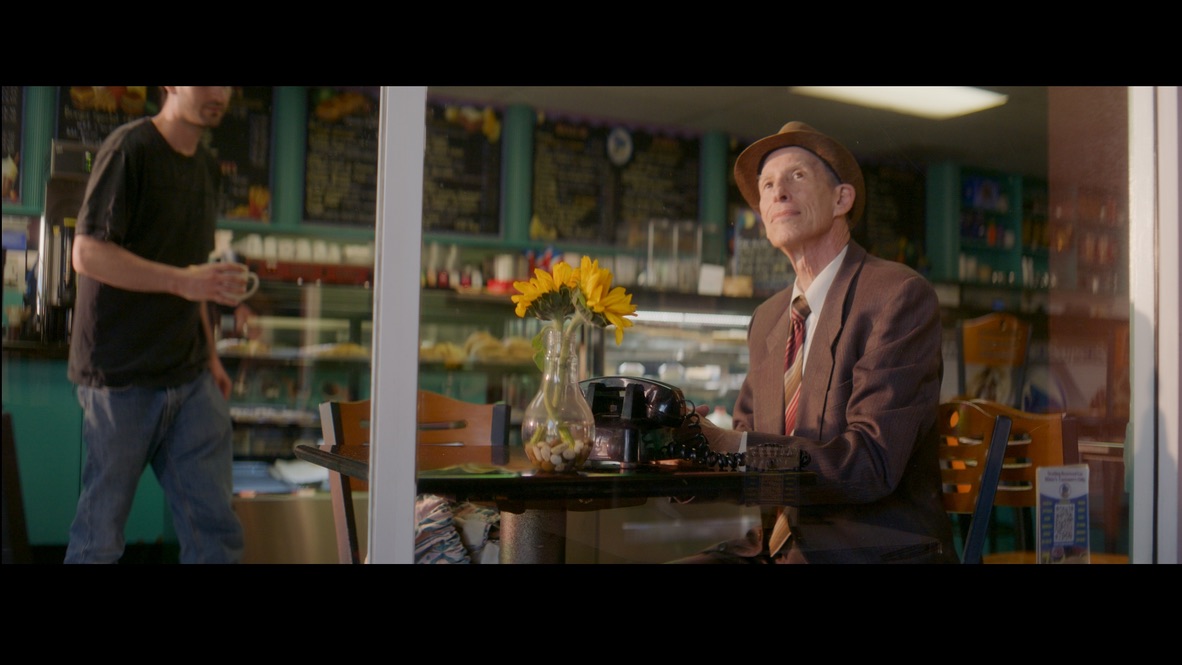 An older man with a rotary phone at a café table