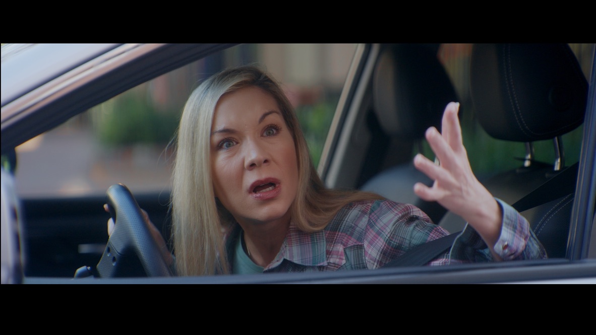 A woman gesturing from the driver’s seat of a car