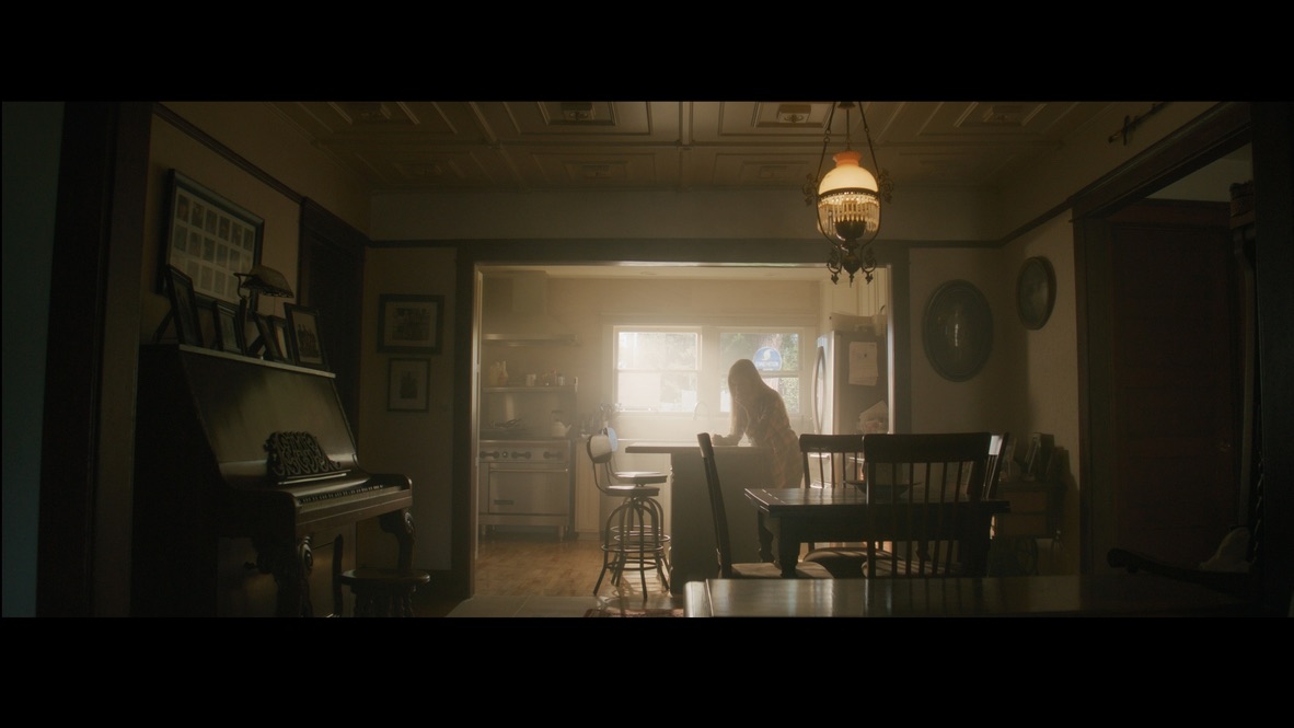 A woman in a sunlit kitchen beyond a dining room