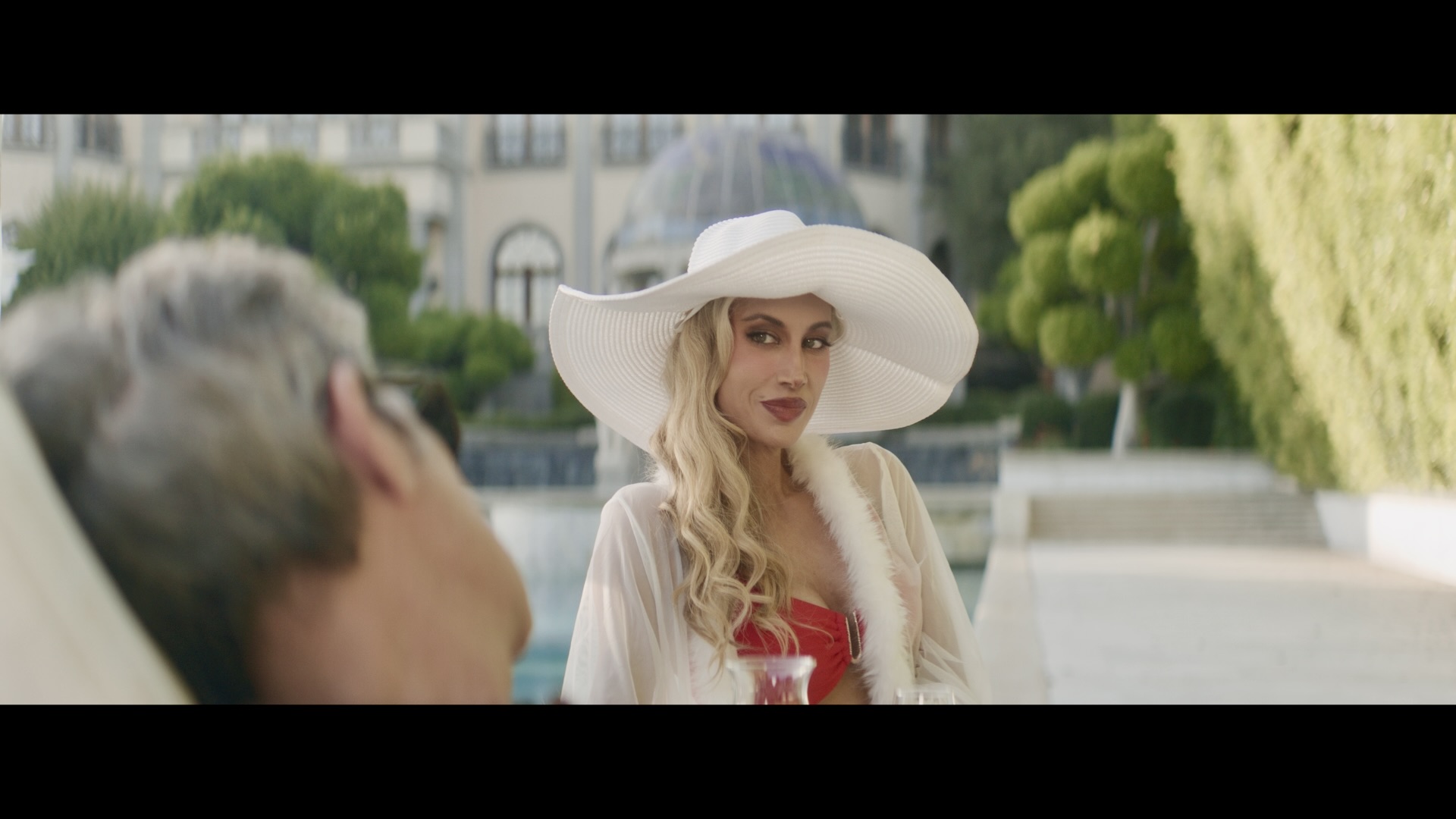A woman in a wide white hat seated across from a man outdoors