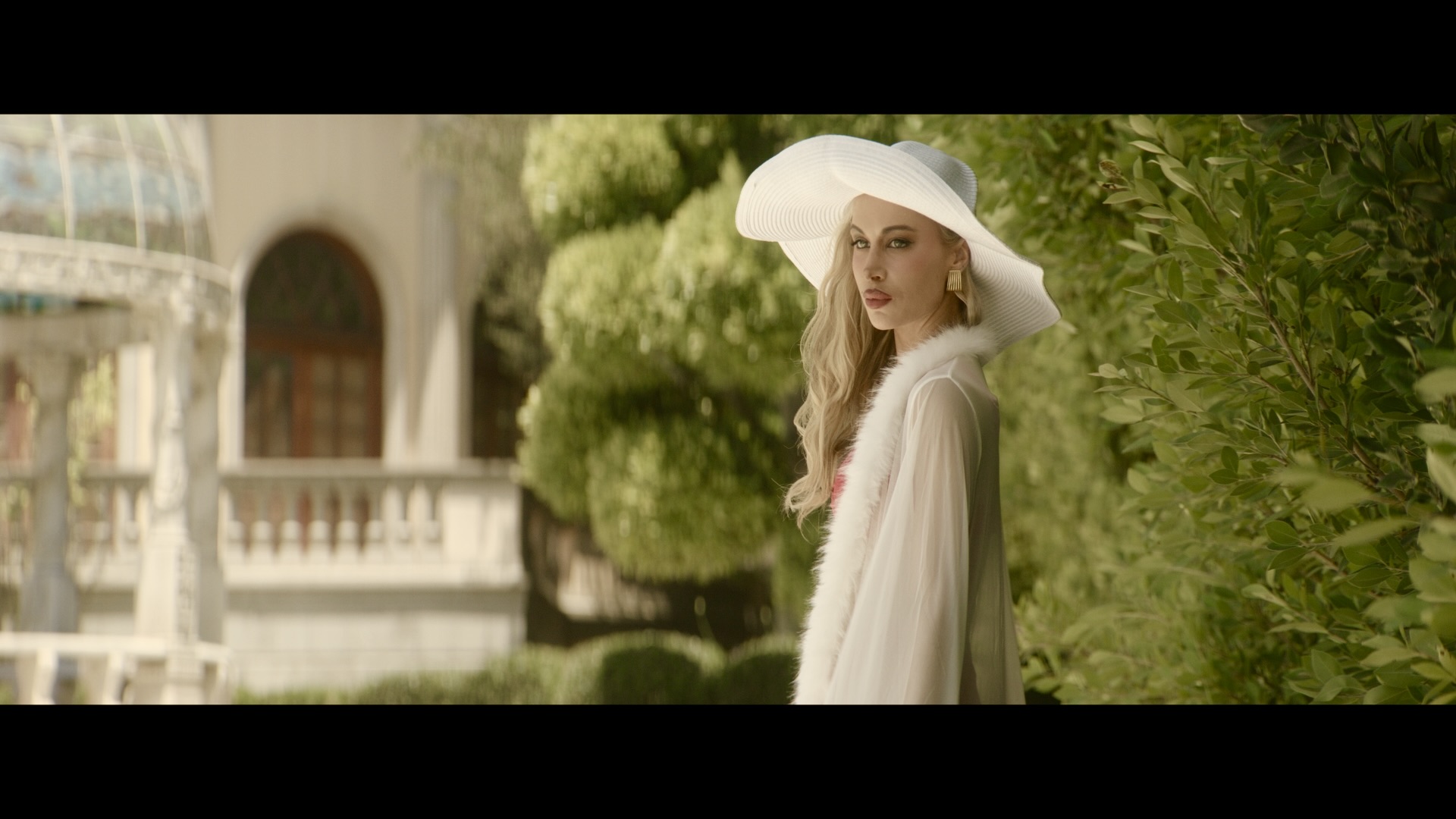 A woman in a white hat beside a hedge and estate