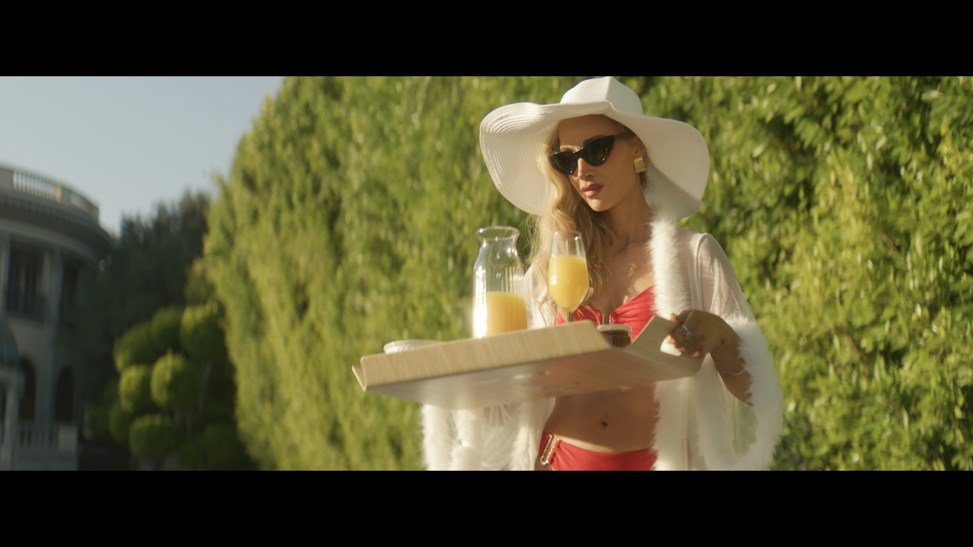 A woman wearing a white hat and sunglasses carrying a breakfast tray